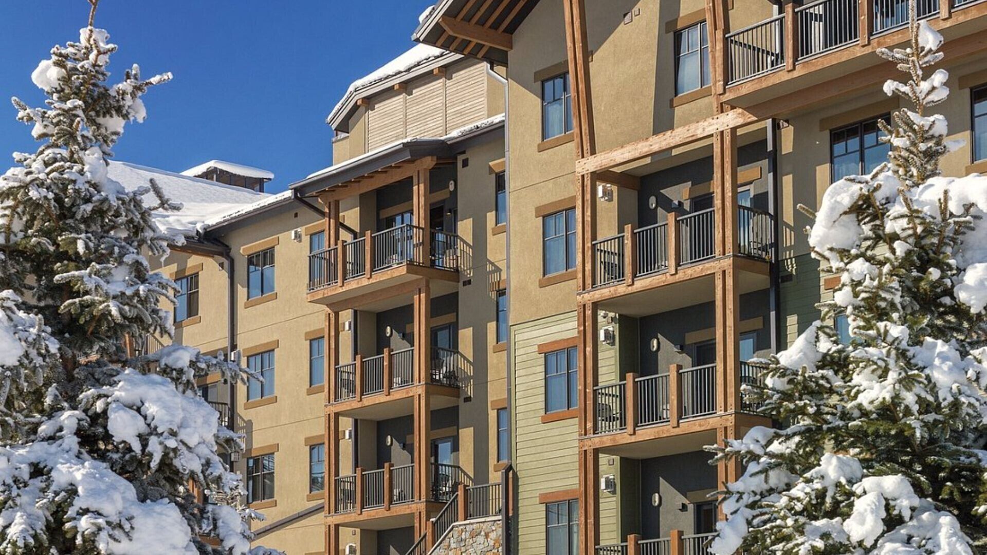 Un hotel de varios pisos con balcones, árboles cubiertos de nieve y un cielo azul despejado.