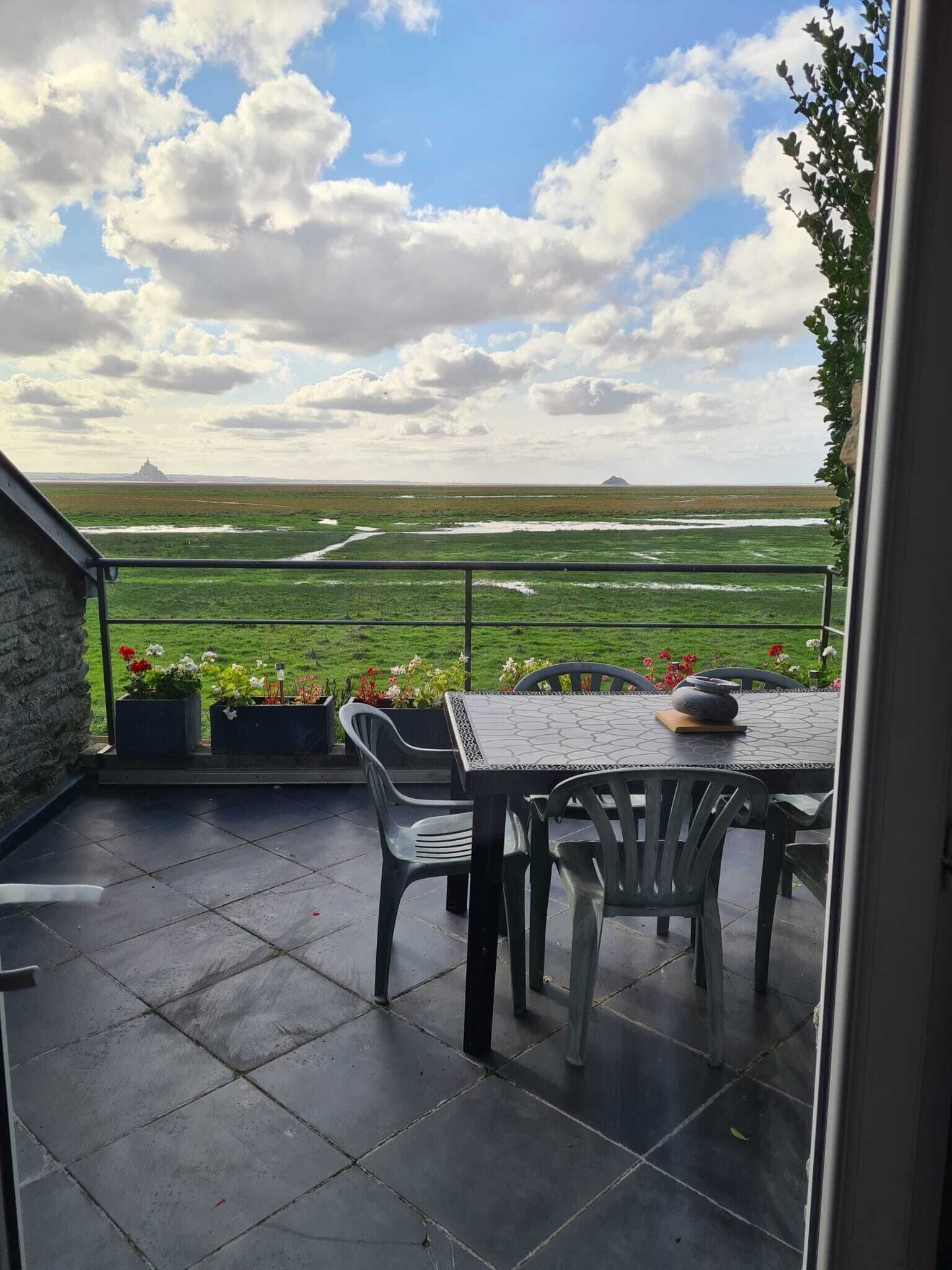 Une terrasse avec une table et des chaises, un mur en pierre et une vue sur un champ verdoyant et des collines lointaines.