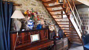 Una stanza rustica con parete in pietra, scala in legno, un comò di legno, una lampada e un vaso con fiori.