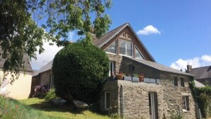 Una casa in pietra con tetto spiovente, un grande albero nel giardino e un cielo azzurro intenso.