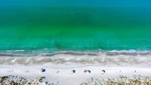 An aerial view of a beach with clear turquoise water, white sand, and several beach umbrellas. - Perfect Beach View 2 Bedroom Condo (Longboat Key)