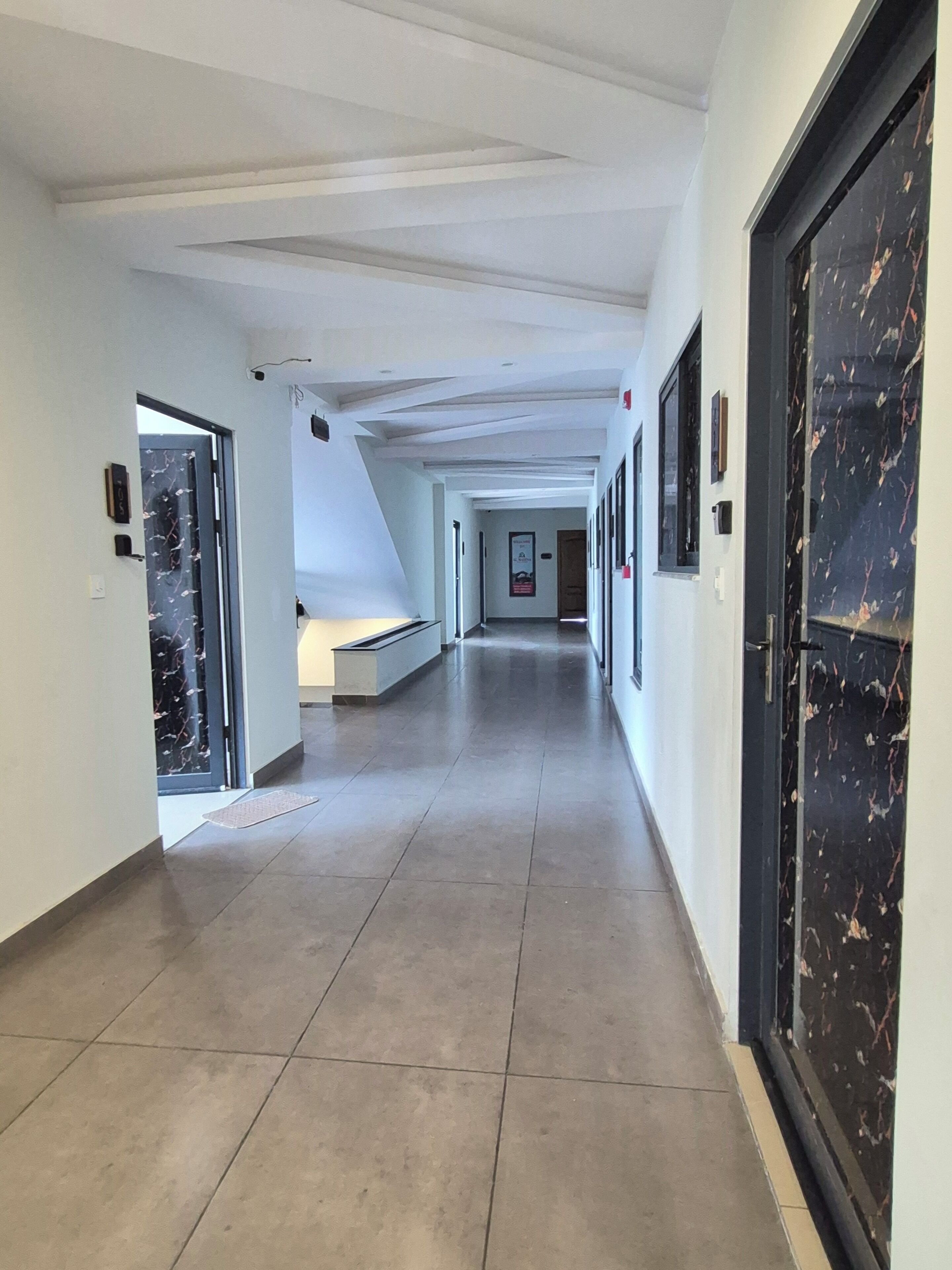 A corridor with a tiled floor, white walls, and doors on both sides.