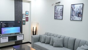 Moderni olohuone, jossa on harmaa sohva, litteänäyttöinen televisio ja seinällä tauluja.