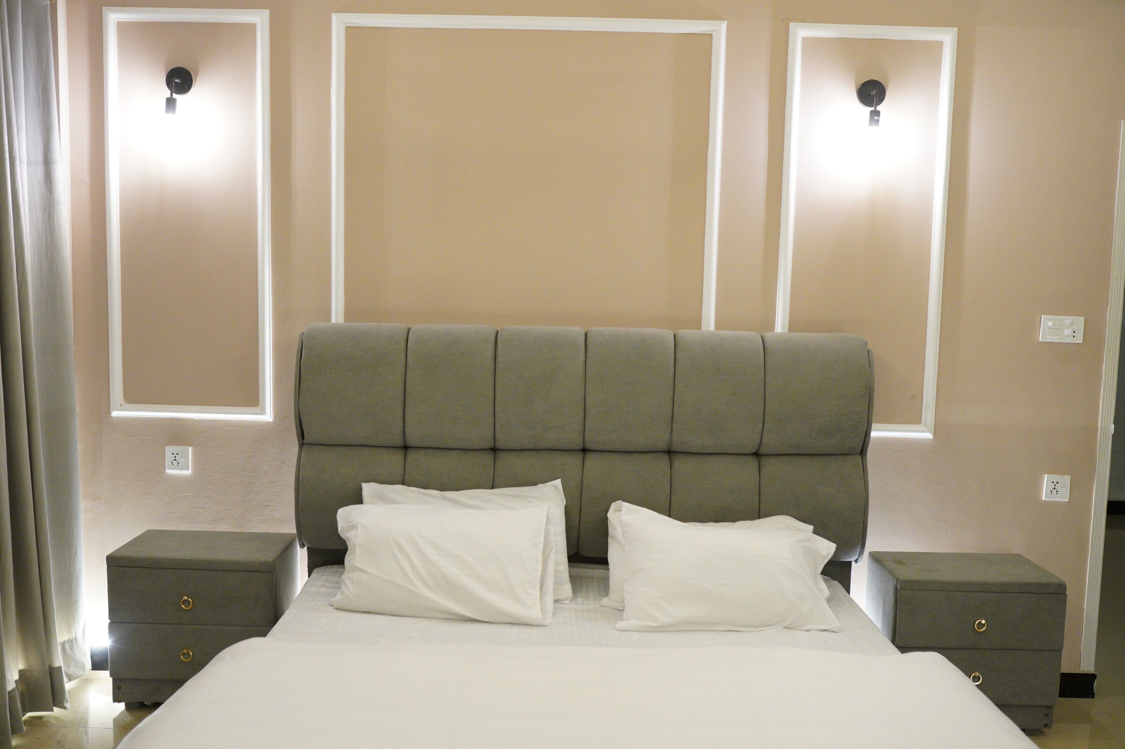 Une chambre d’hôtel avec un grand lit, deux tables de chevet et des lampes fixées au mur.