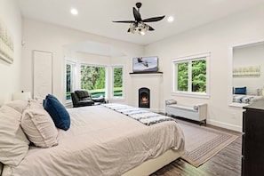 A bedroom with a bed, a fireplace, a TV, and large windows.
