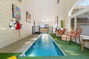 A narrow indoor pool with artificial turf, surrounded by walls with framed artwork, and equipped with a lifebuoy and a pool ladder.