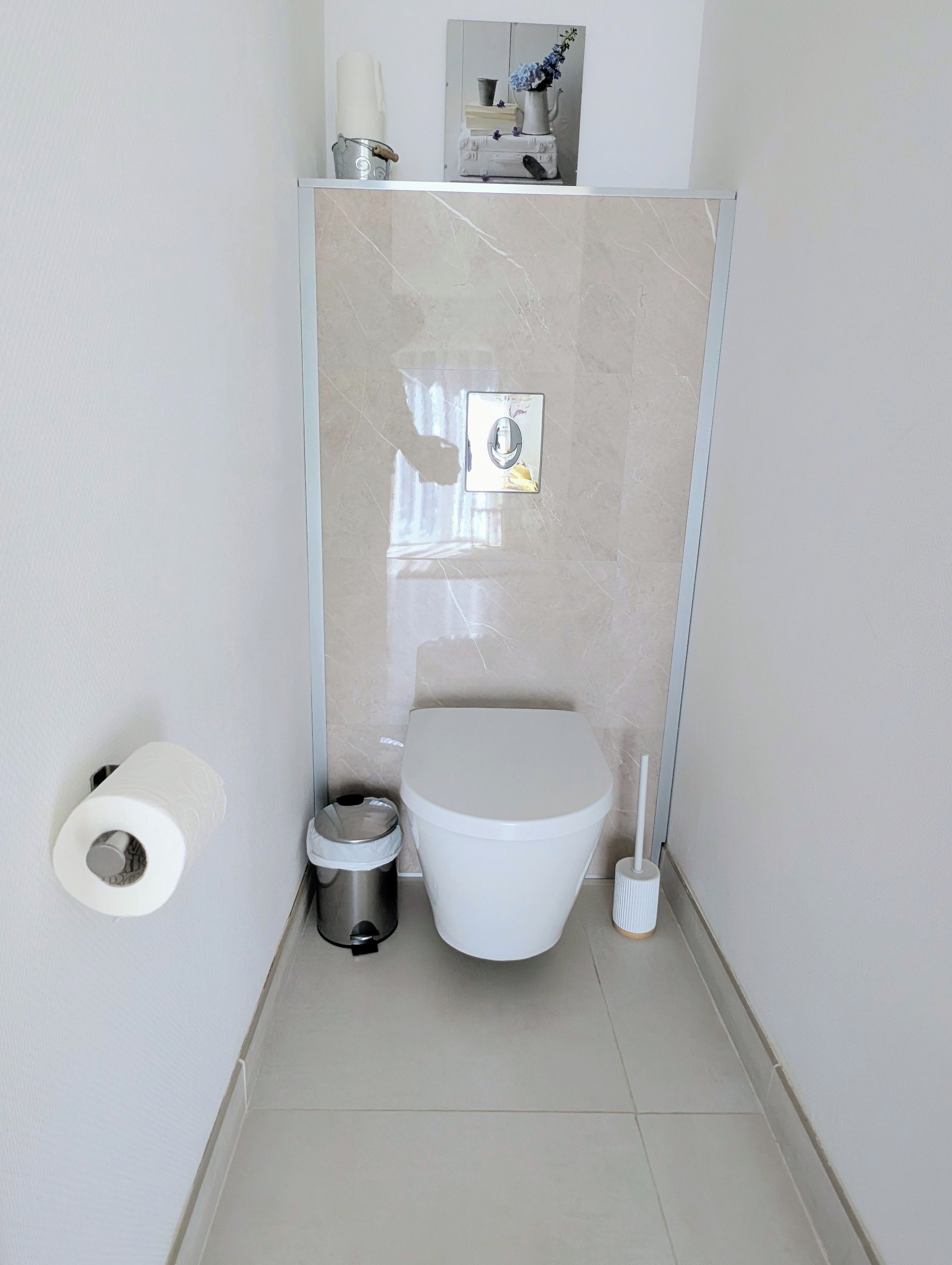 Ein kleines Badezimmer mit Toilette, Mülleimer und Toilettenpapierhalter.