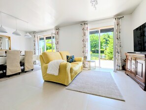 Olohuone, jossa on keltainen sohva, televisio ja suuri ikkuna, jossa on verhot.