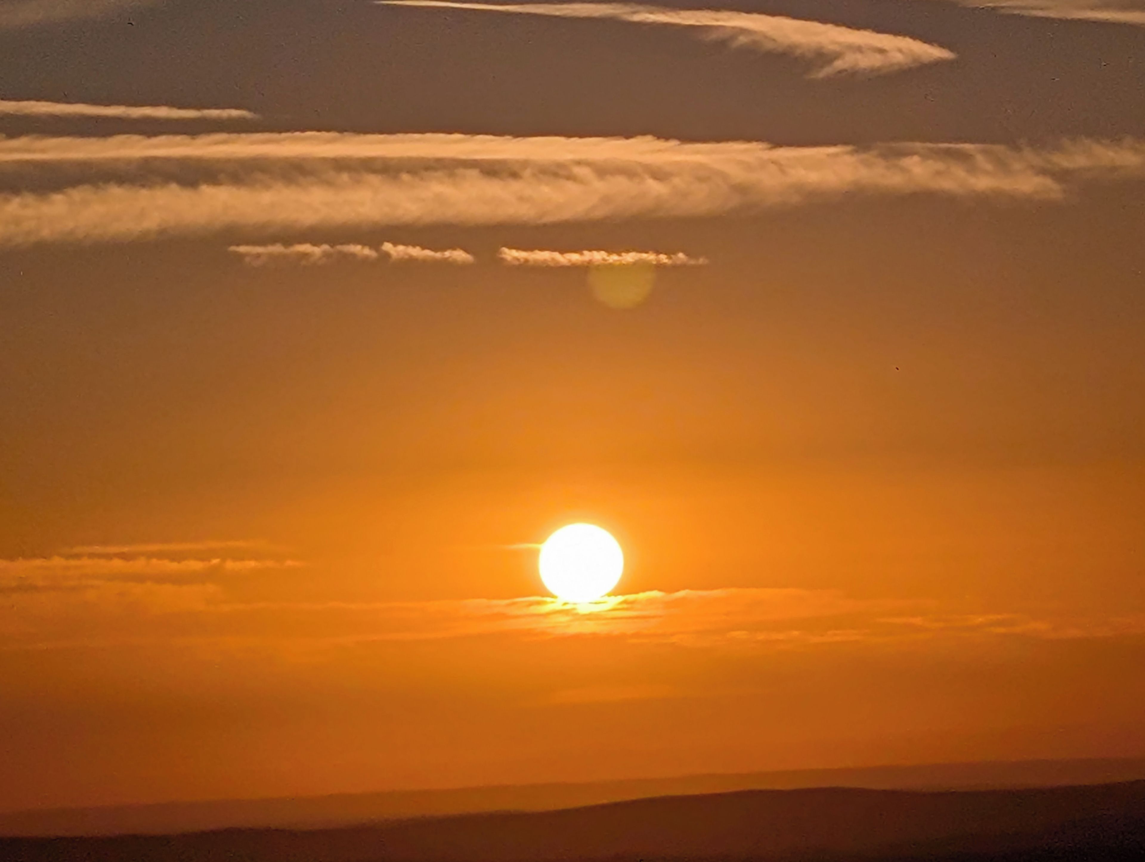 Ein Sonnenuntergang mit tiefstehender Sonne, Wolken am Himmel und einer Landschaftssilhouette.