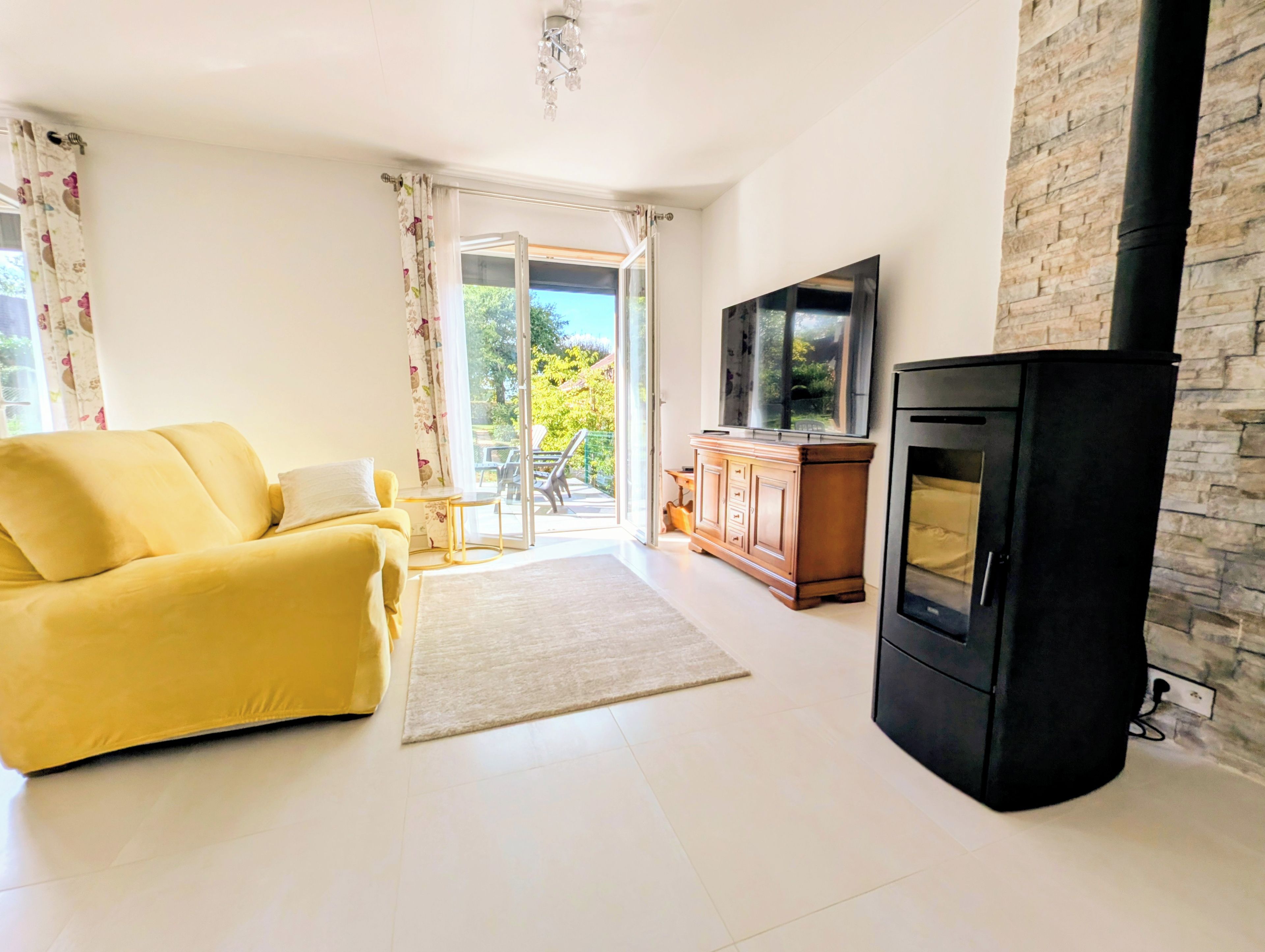 A living room with a yellow sofa, a flat-screen TV, a fireplace, and a sliding glass door leading to an outdoor area.