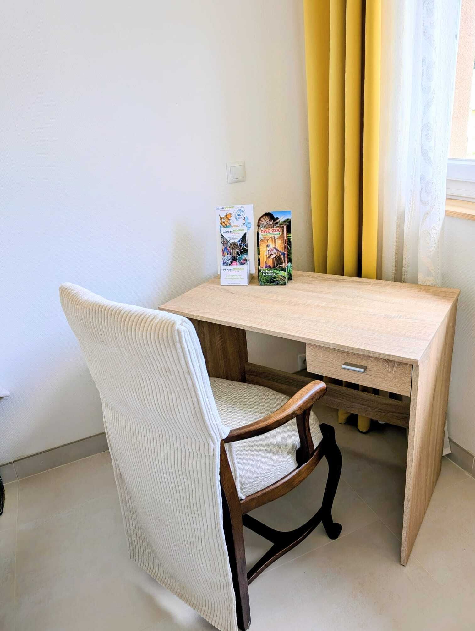 A wooden desk with two books, a white chair, and yellow curtains.