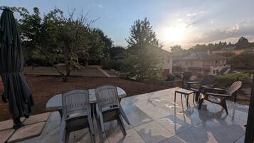 Een terras buiten met een tafel, stoelen, een parasol en huizen op de achtergrond.