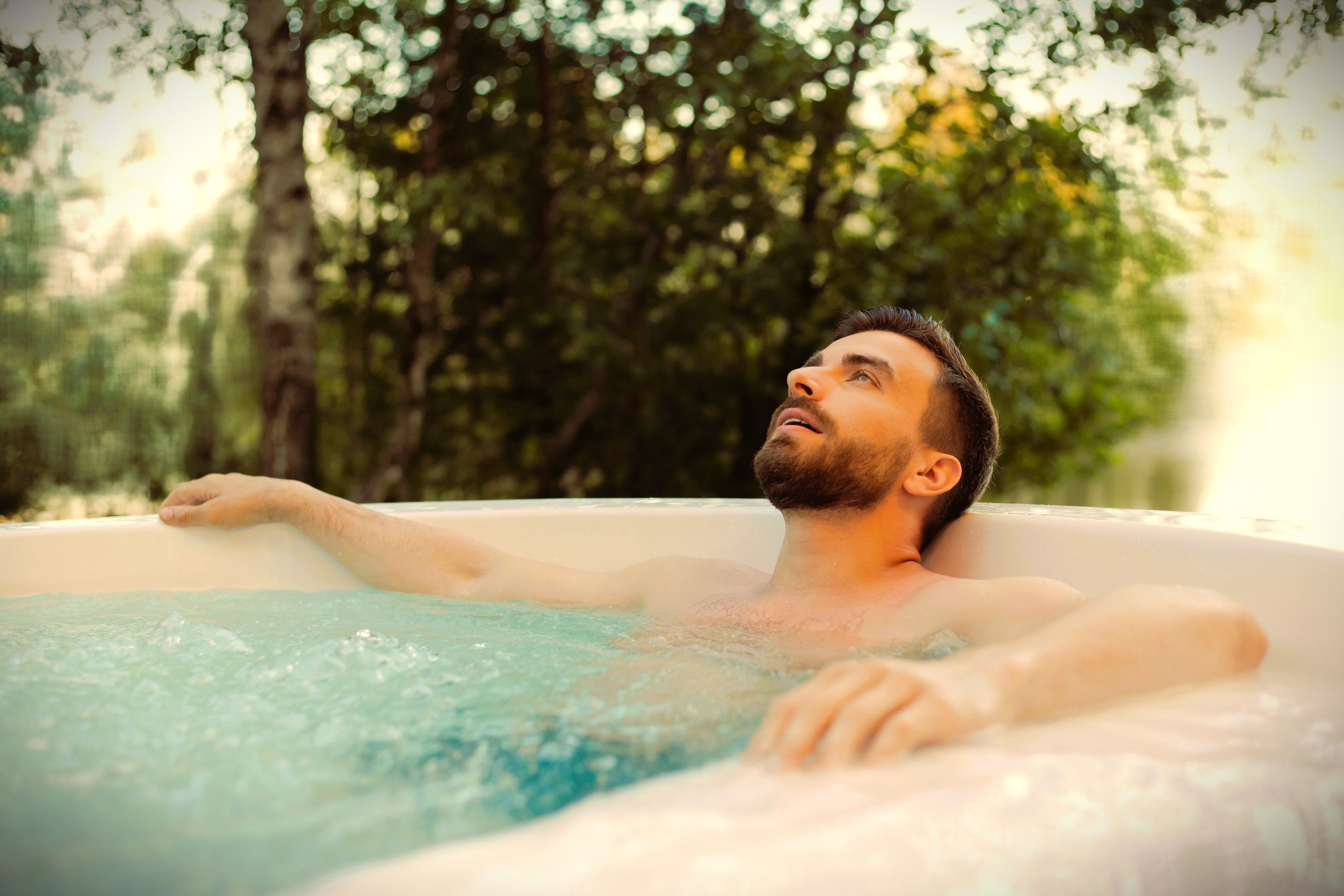 A person relaxing in a hot tub outdoors surrounded by trees.