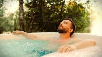 A person relaxing in a hot tub outdoors surrounded by trees.