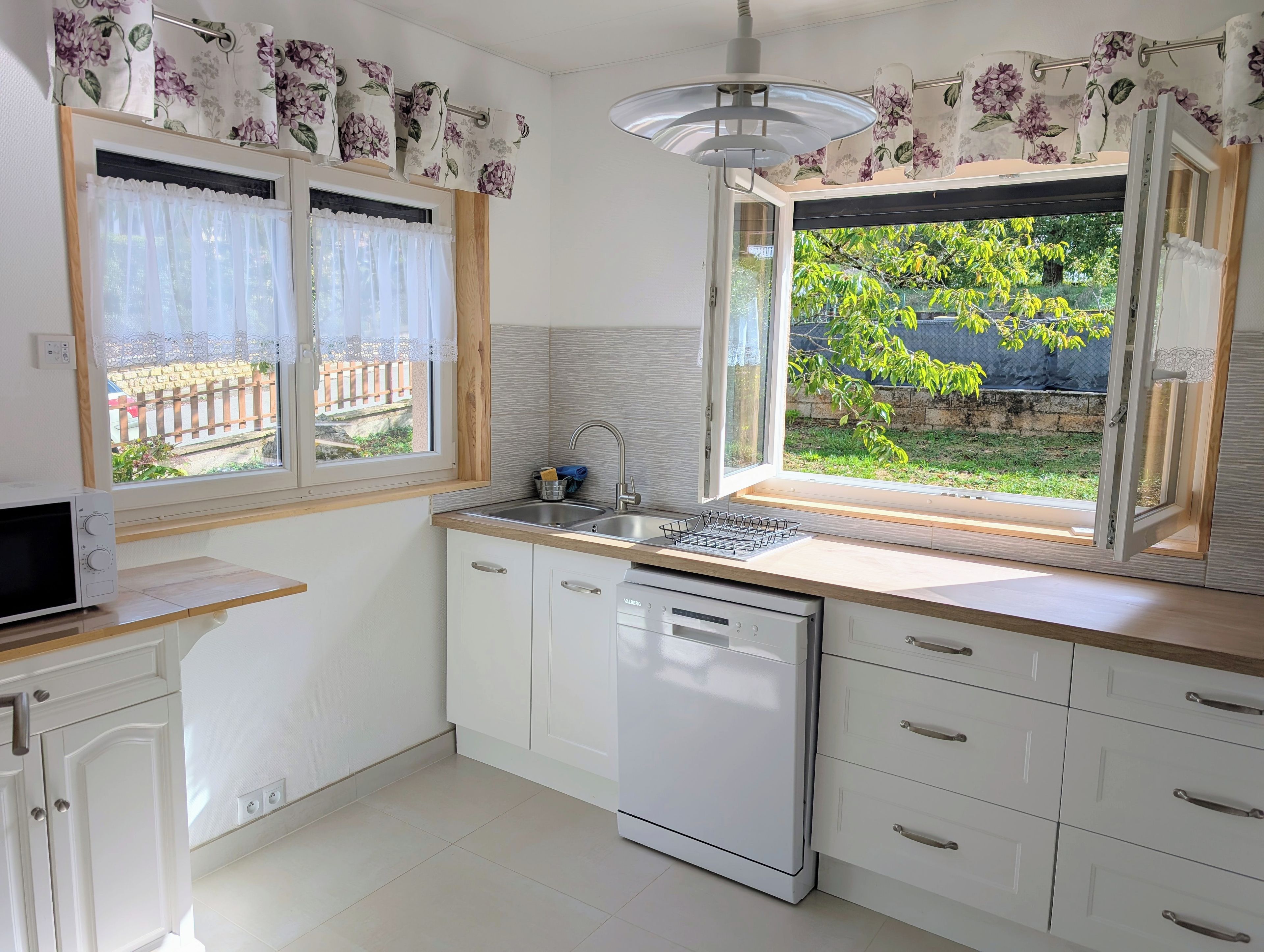 A kitchen with a dishwasher, a sink, and a window with curtains.