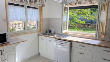 A kitchen with a dishwasher, a sink, and a window with curtains.