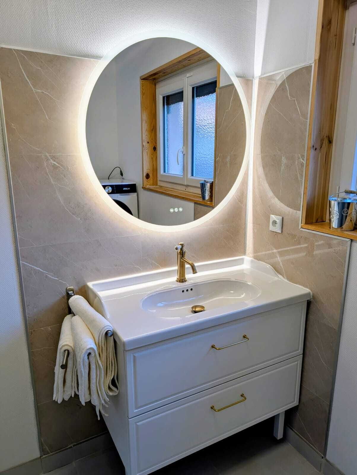 Une salle de bain avec un miroir rond, un lavabo et une fenêtre.