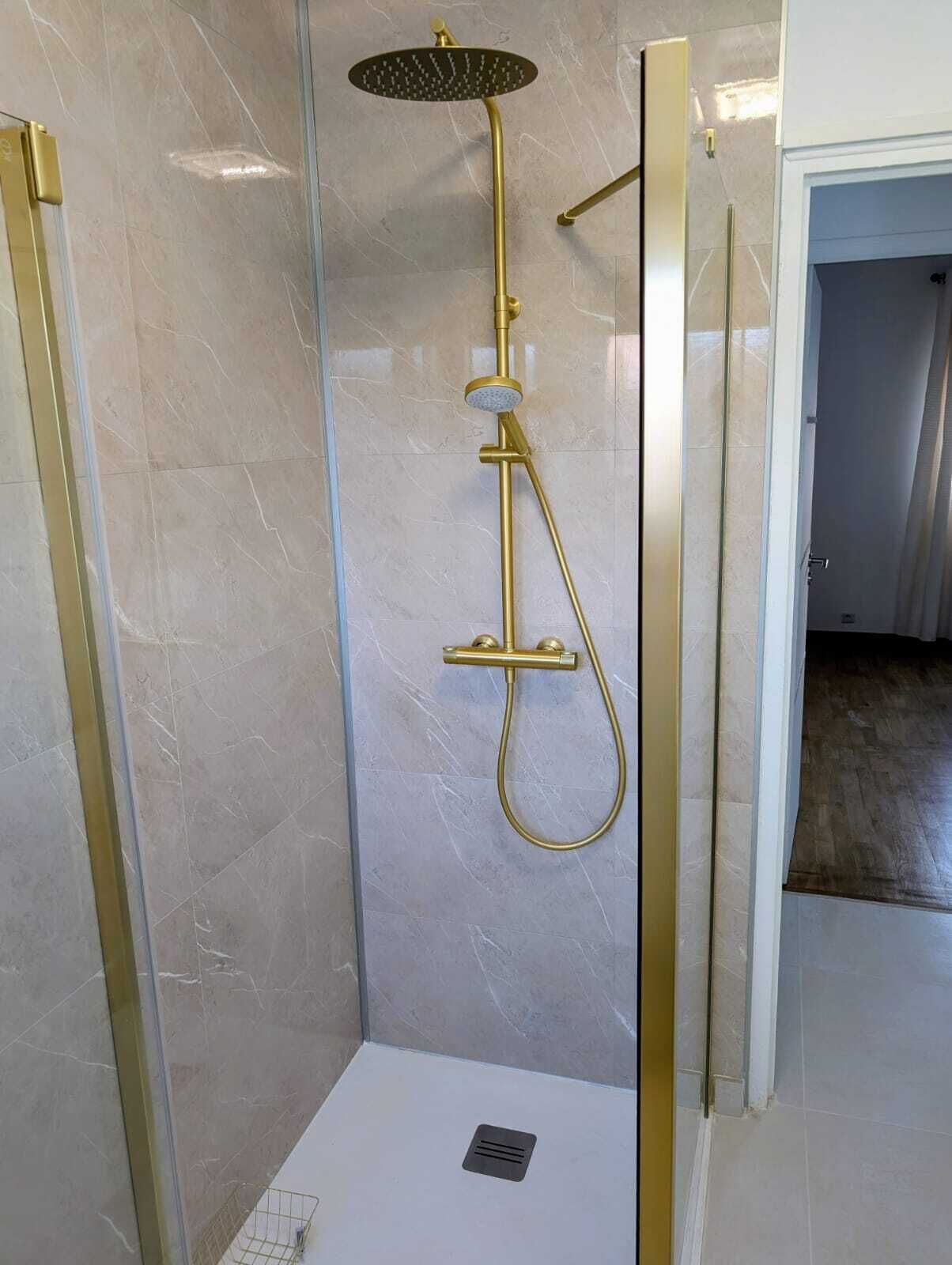 A walk-in shower with a gold showerhead and a handheld shower attachment.