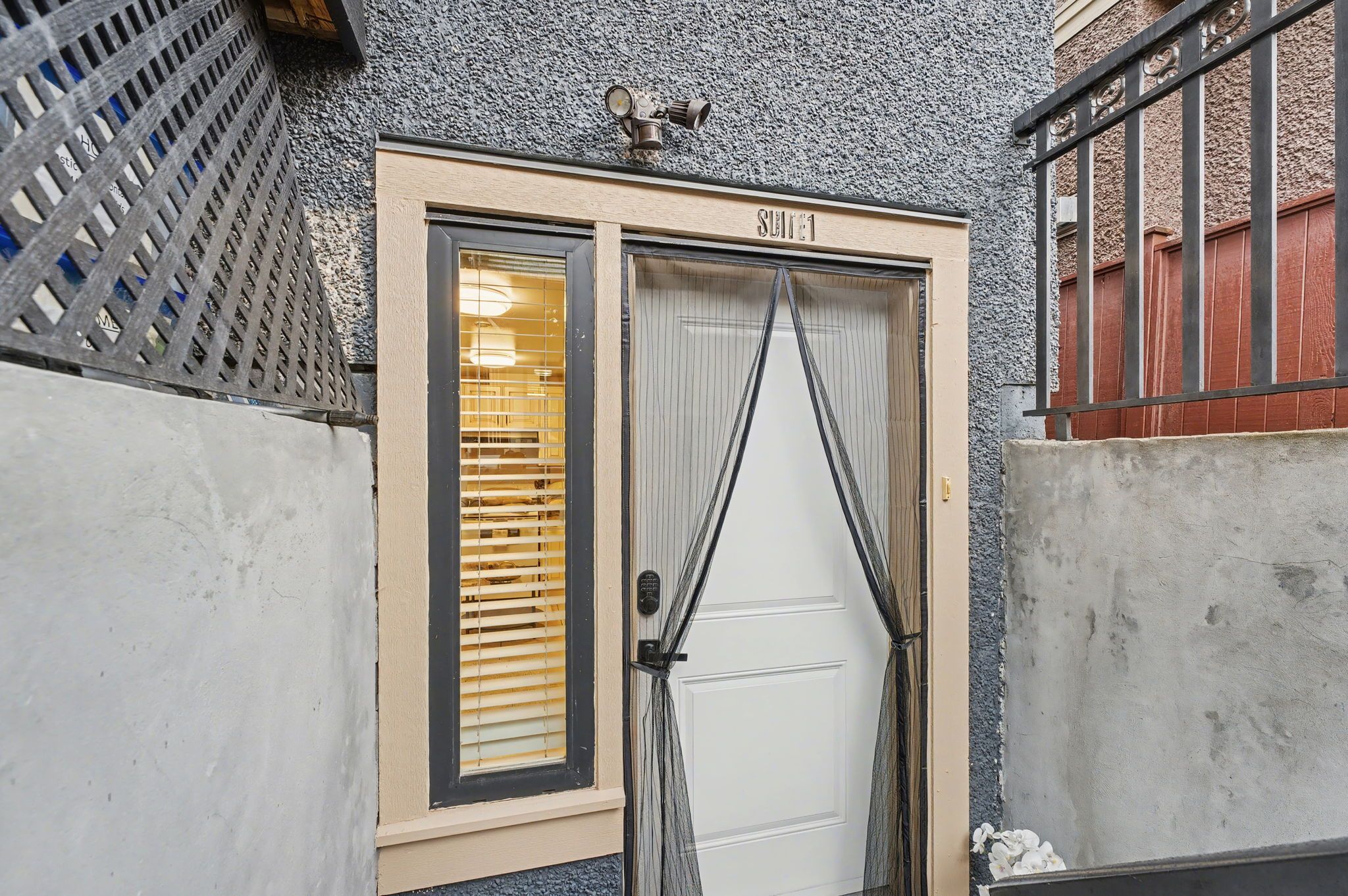 A hotel entrance with a beige door, a security camera above, and a barred gate to the right.