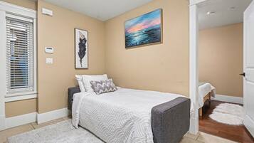 Um quarto com uma cama, um quadro, um termostato e uma janela com persianas.
