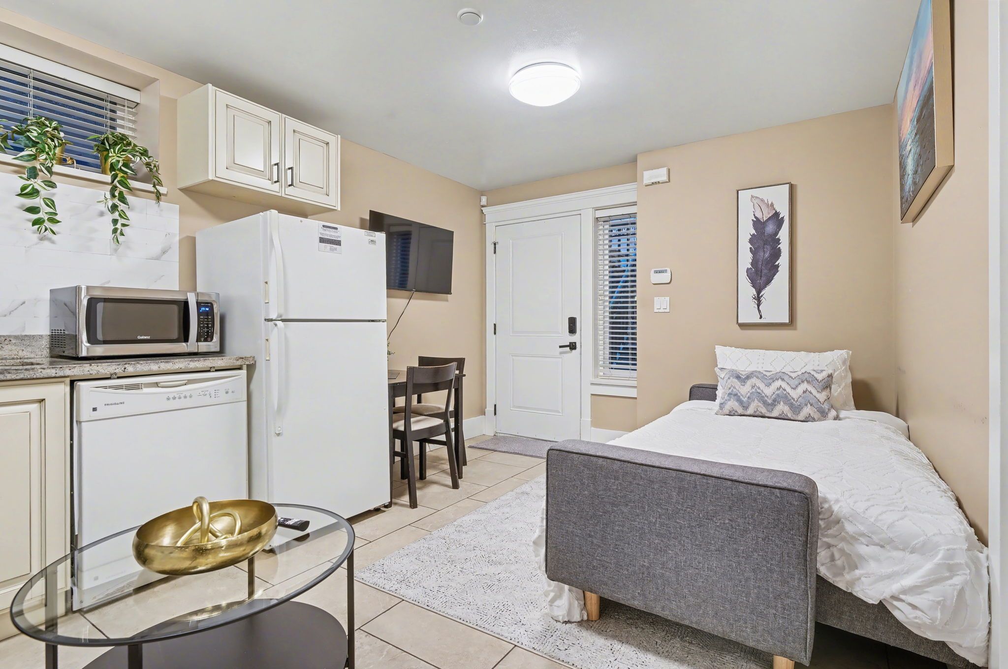 A compact room with a bed, a small kitchenette, a dining area, and a window with blinds.