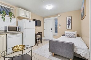 A compact room with a bed, a small kitchenette, a dining area, and a window with blinds. - Comfy 1 Bedroom Suite by Mroke Vacations (Vancouver)
