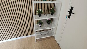 Un coin avec une étagère en métal blanc où sont disposées des plantes en pot, une lampe verte et un tableau de distribution électrique blanc.