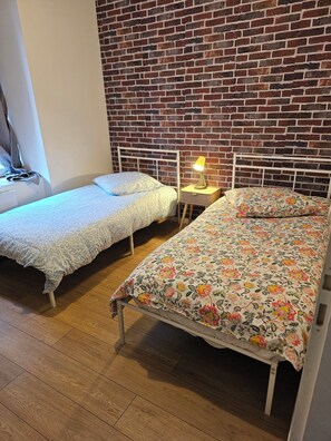 A room with two single beds, a brick wall, and a wooden floor. - T3 in the historic heart of Montluçon, train station 10 min away (Montluçon)