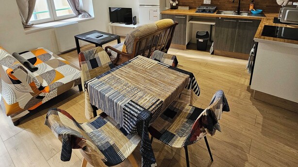Un salon moderne avec un canapé, une table basse à motifs et un coin repas avec des chaises. On y trouve également une cuisine avec des meubles en bois et un four à micro-ondes.