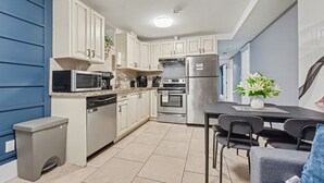 A modern kitchen with white cabinets, a stainless steel refrigerator, a microwave, and a dishwasher. There is a dining table with chairs and a potted plant. - Quiant 2 Bedroom Suite by Mroke Vacations (Vancouver)