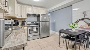 A modern kitchen with stainless steel appliances, a dining area with a table and chairs, and light blue walls. - Quiant 2 Bedroom Suite by Mroke Vacations (Vancouver)