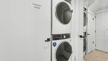Un cuarto de lavandería con dos lavadoras apiladas, un cartel que indica el lugar y una puerta que da a otra zona.