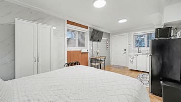 Ein Schlafzimmer mit einem Bett, einem kleinen Esstisch mit Stühlen, einer Küchenzeile mit Kühlschrank und einem Badezimmer mit Toilette.