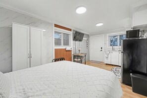Une chambre avec un lit, une petite table à manger avec des chaises, un coin cuisine avec un réfrigérateur et une salle de bain avec des toilettes.