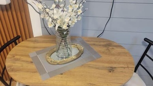 Una mesa redonda con un florero, un marco decorativo y un mantel individual.