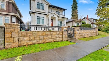 A two-story house with a stone wall, a gated driveway, and a sidewalk.