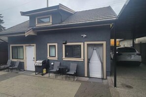 A two-story building with a garage, a covered outdoor seating area, and a car parked inside. - Secluded Bachelor Suite by Mroke Vacations (Vancouver)