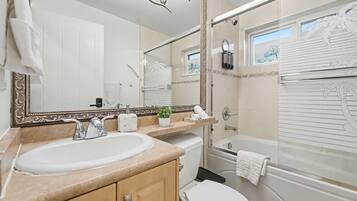 A bathroom with a large mirror, a sink, a toilet, and a shower area.