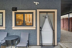 A building exterior with a textured facade, a door labeled 'Bachelor Suite 6363,' and two outdoor tables with chairs. - Secluded Bachelor Suite by Mroke Vacations (Vancouver)