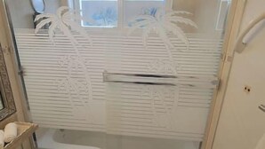 Un baño con cabina de ducha de vidrio satinado, una bañera blanca y un espejo en la pared.