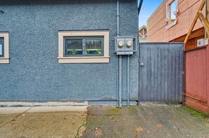 A building exterior with a textured blue wall, two windows with beige frames, a grey door, and a red fence. - Secluded Bachelor Suite (Vancouver)