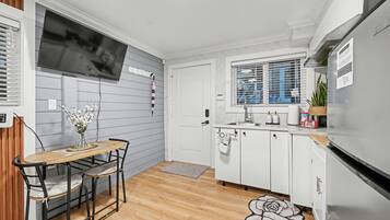 Eine kleine Küche mit Esstisch, einem darüber montierten Fernseher und einem Kühlschrank.