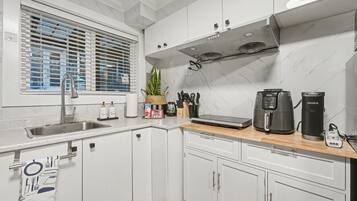 A modern kitchen with white cabinets, a stainless steel sink, a window with blinds, a coffee maker, and a kettle.