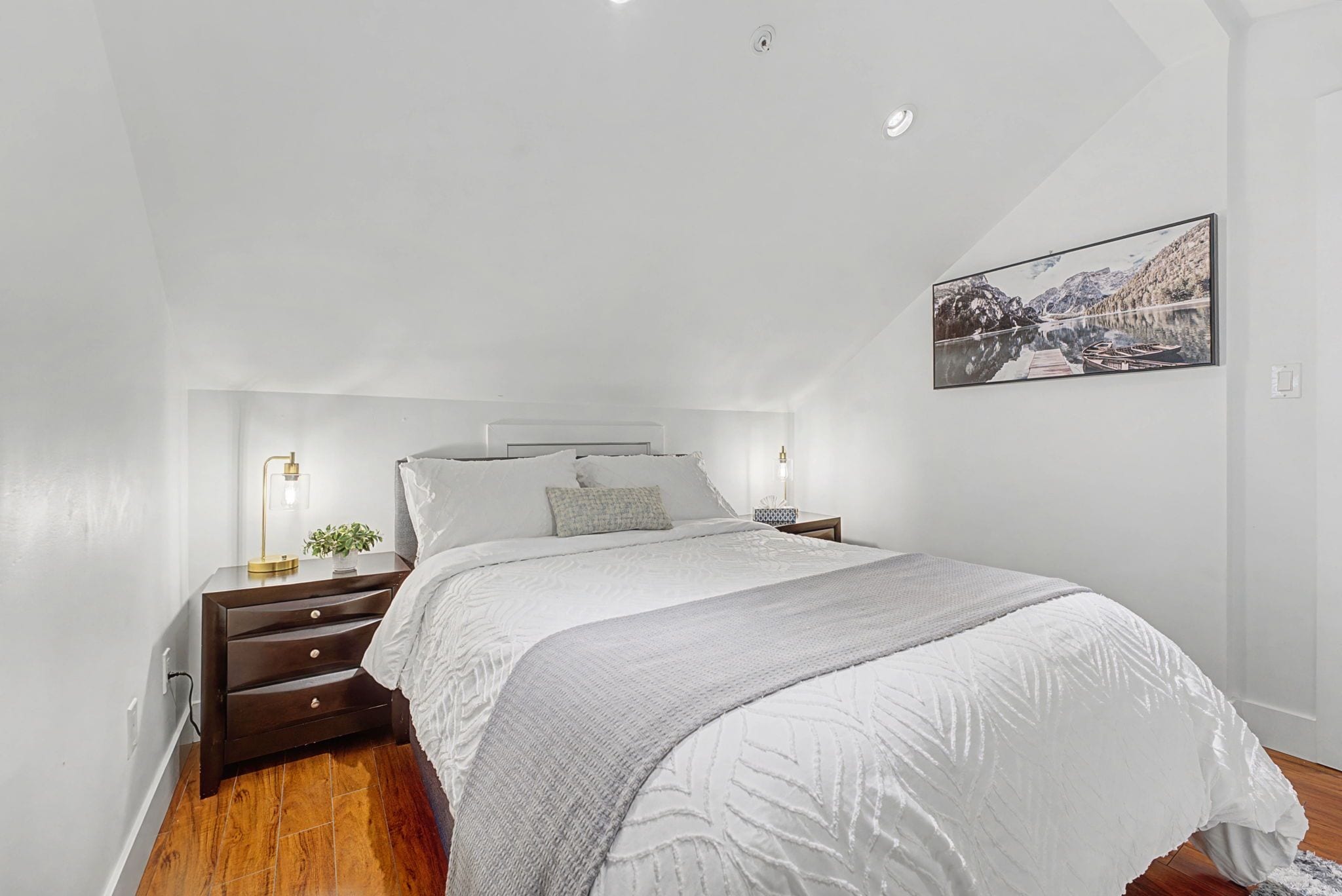Ein Schlafzimmer mit Bett, Nachttischen, einem Wandbild und Holzboden.