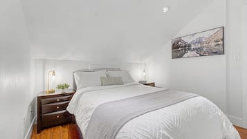 Ein Schlafzimmer mit Bett, Nachttischen, einem Wandbild und Holzboden.