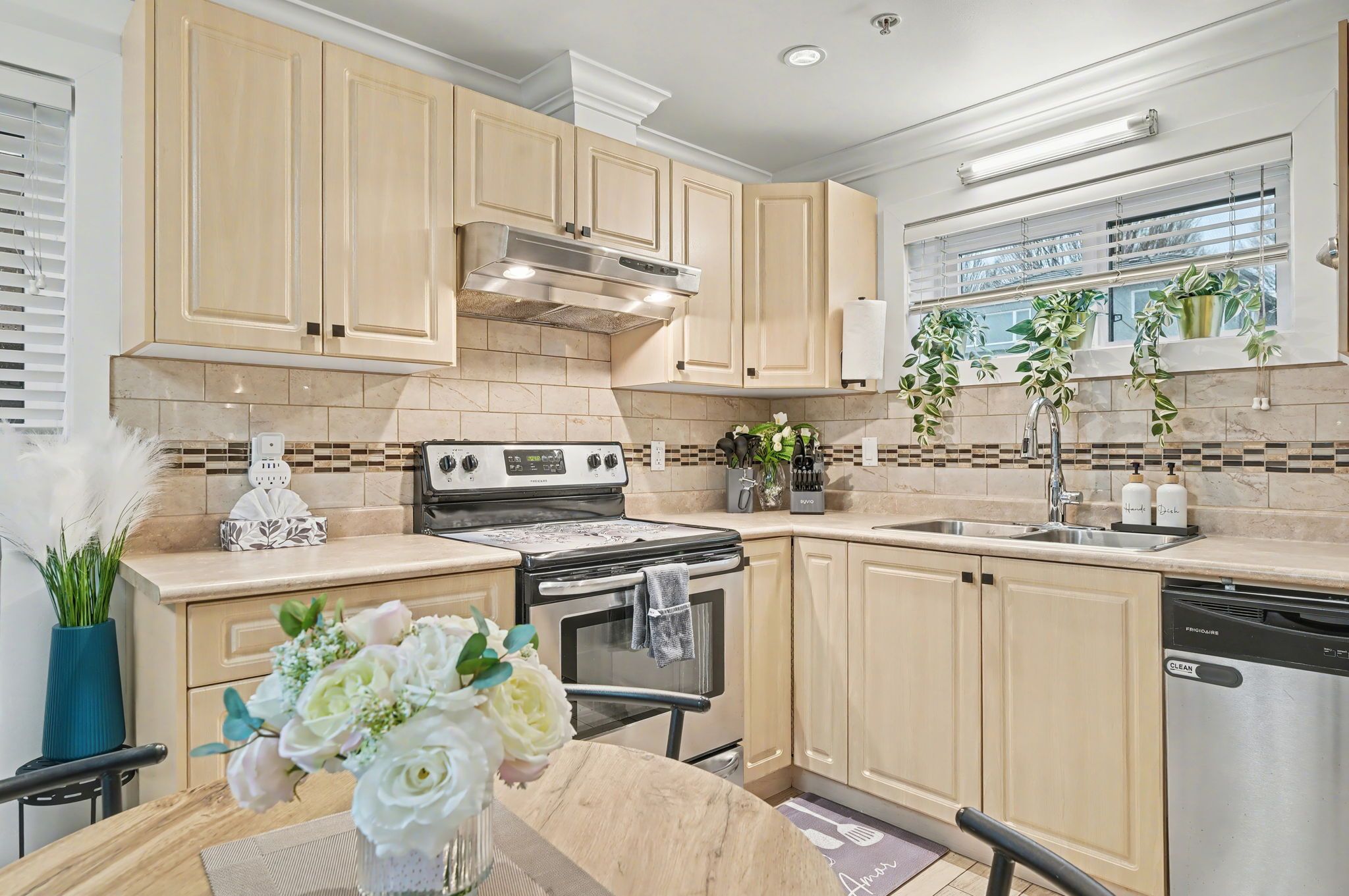 A modern kitchen with light wood cabinets, a stainless steel stove, and a dishwasher.