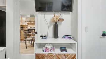 A modern kitchen with a flat-screen TV, a vase with dried plants, and a dining area with chairs and a table.