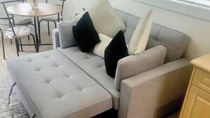 Ein graues Sofa mit passendem Hocker, ein kleiner runder Tisch und ein Stuhl in einem Zimmer mit Holzboden.