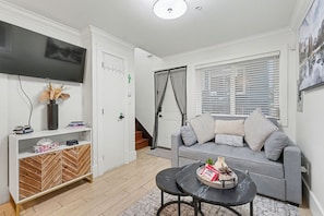 A living room with a grey sofa, a black coffee table, a TV mounted on the wall, and a staircase leading to another level.