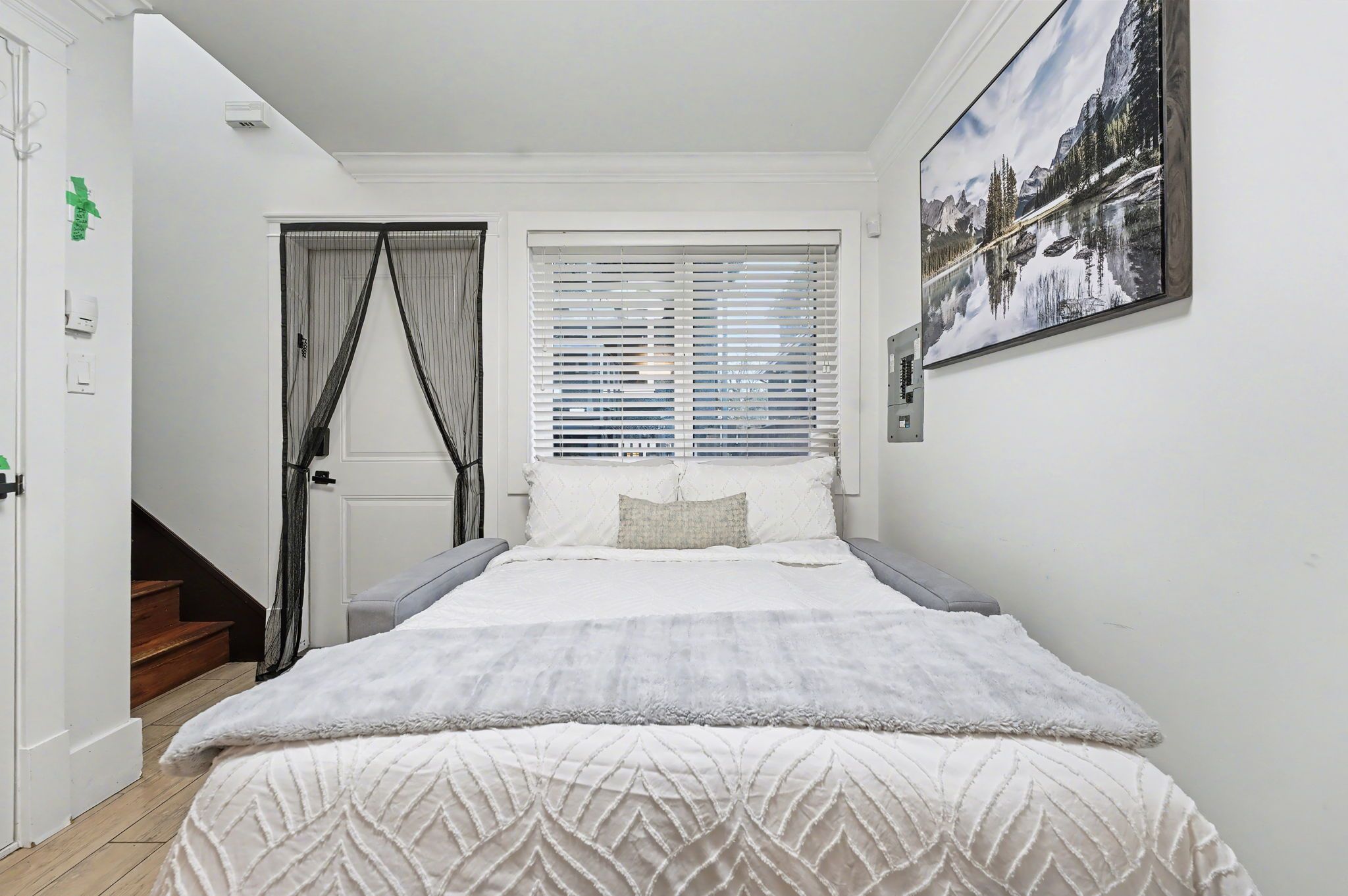 A bedroom with a bed, a window with blinds, a staircase, and a door.